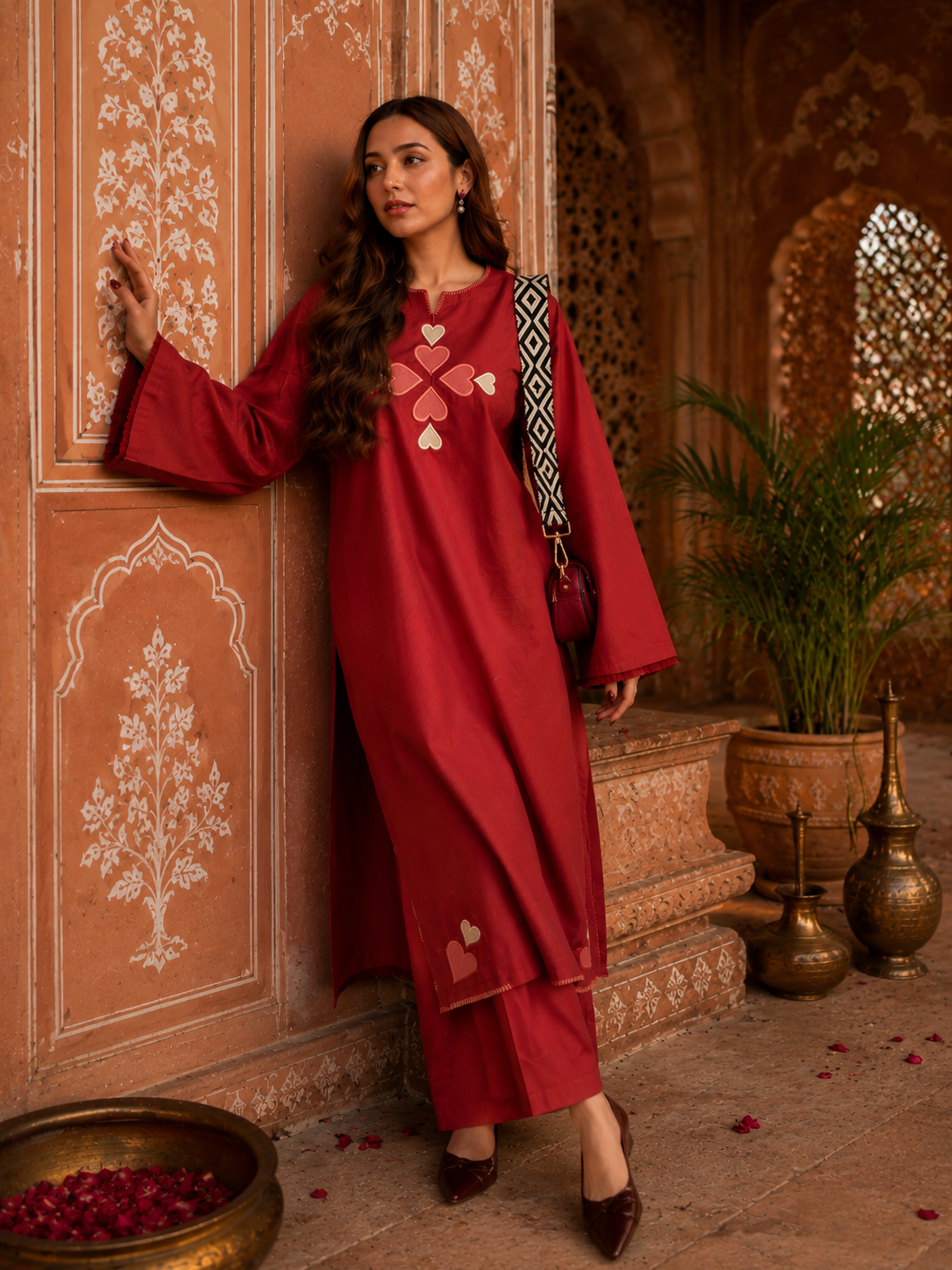 Woman wearing red cotton Pakistani style co-ord set with heart embroidery standing beside textured wall